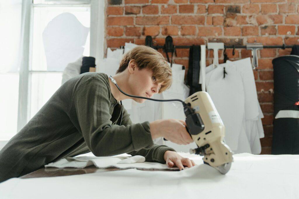 pexels-photo-4621908-4621908 A focused young designer uses a rotary cutter on fabric in a brick-walled studio.