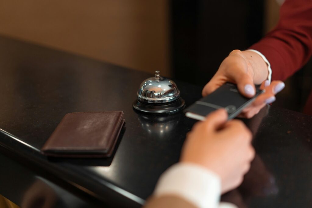 pexels-photo-7820326-7820326 A close-up of a hotel check-in process with a smartphone and card transaction at the reception desk.